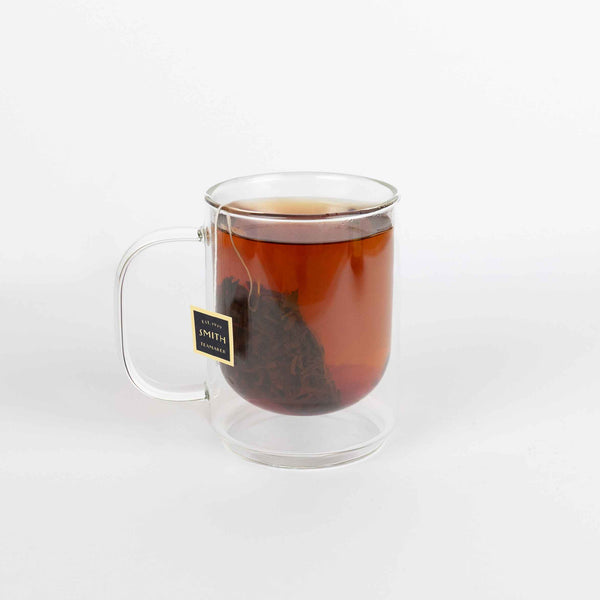 Clear glass mug with tea and a visible brand label on a white background