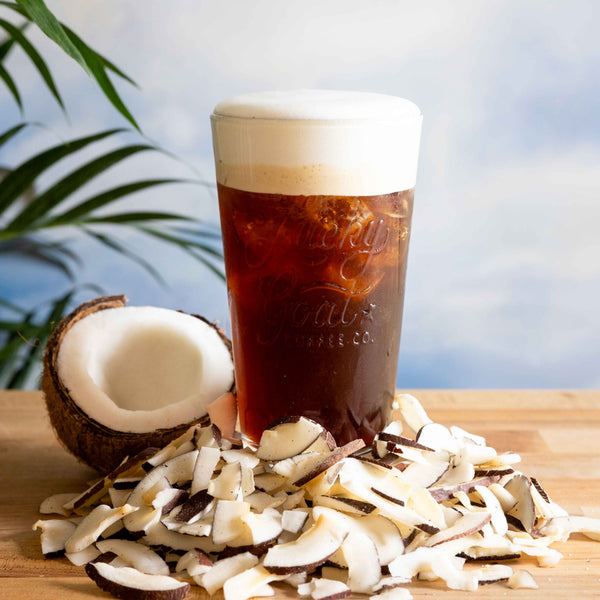 Glass of iced coffee with a coconut and coconut flakes on a wooden surface