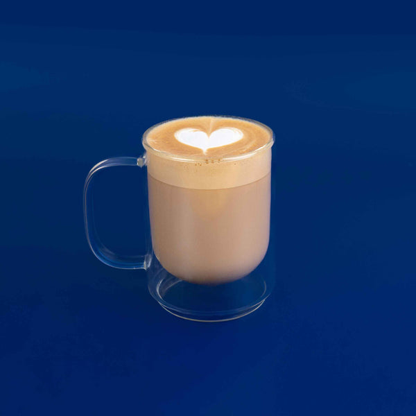 Clear mug with a heart-shaped latte art on a blue background