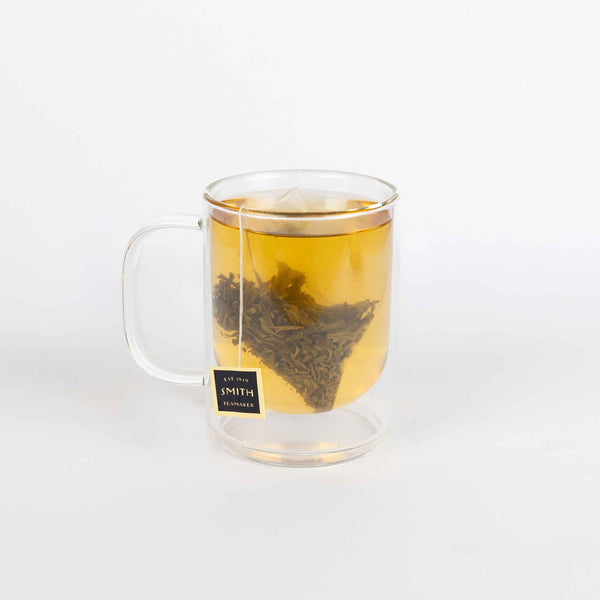 Clear glass mug with tea bag and brewed tea on a white background