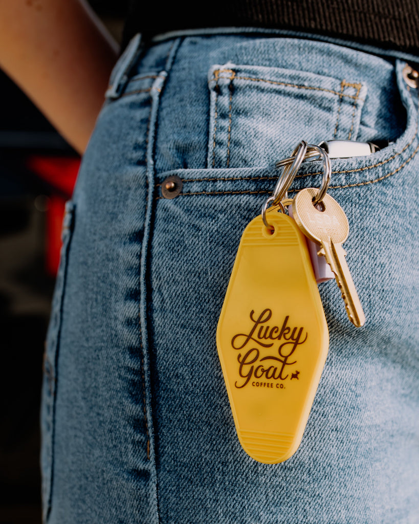 Yellow keychain with 'Lucky Goat' branding attached to a key on blue jeans.