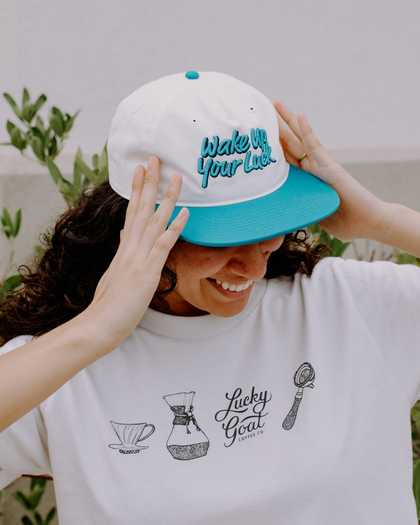 Person wearing a white cap with blue brim and text, and a white t-shirt with graphics and text.