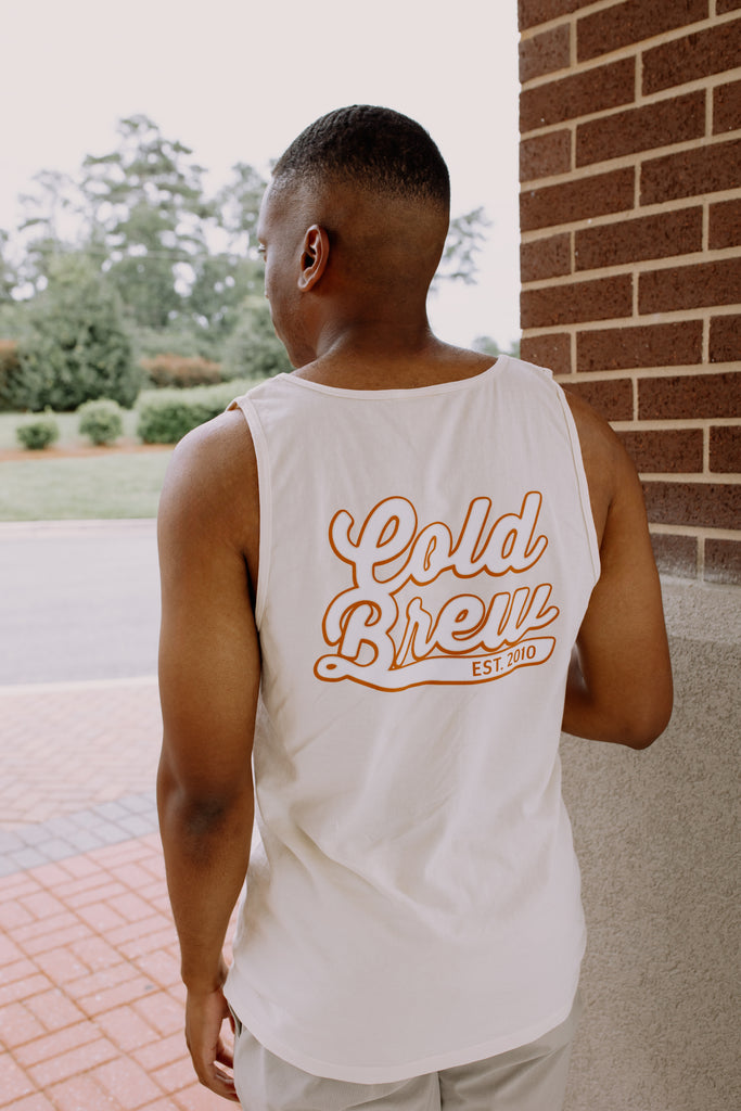 Man wearing a white tank top with 'Cold Brew' text, standing outdoors.