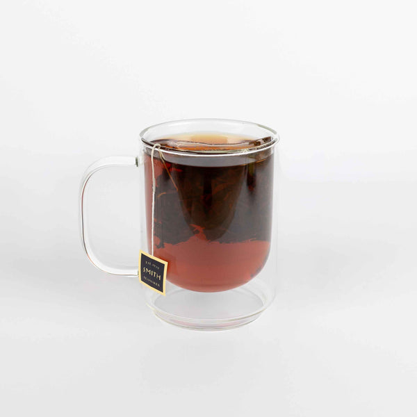Clear glass mug with tea and a tea bag on a white background