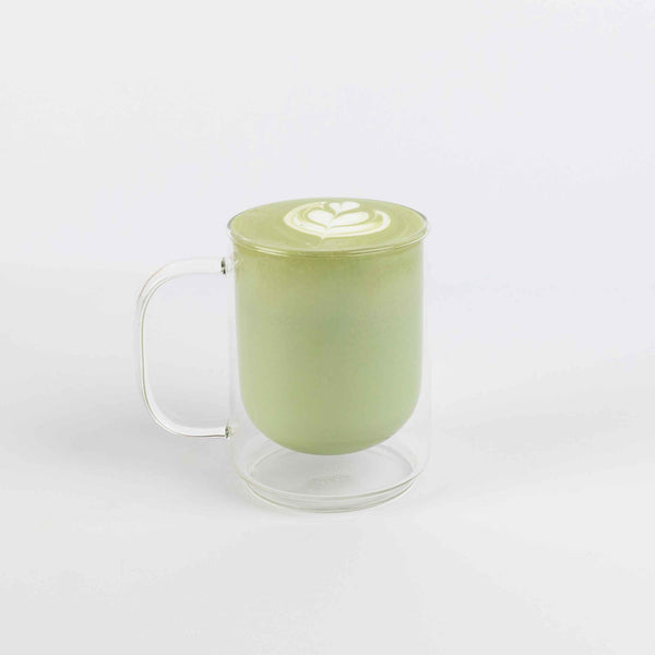 Clear glass mug with green beverage and latte art on a white background