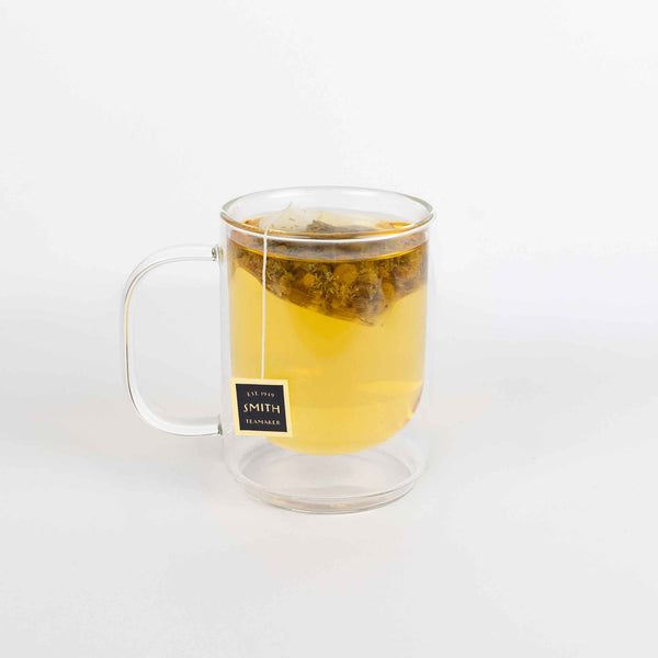 Clear glass mug with tea and a tea bag on a white background
