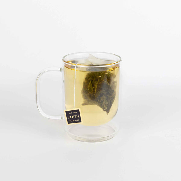 Clear glass mug with a tea bag labeled 'Smith' on a white background