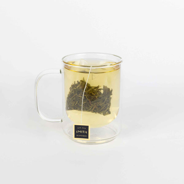 Clear glass mug with a tea bag steeping in hot water on a white background