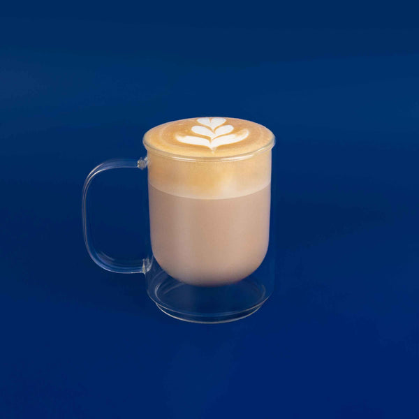 Clear glass mug with a latte art design on a blue background
