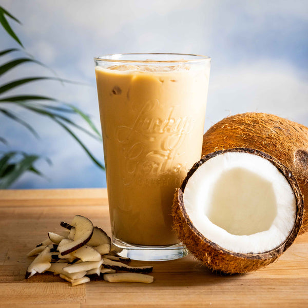 Iced coffee in a glass with a halved coconut and coconut chips on a wooden surface.