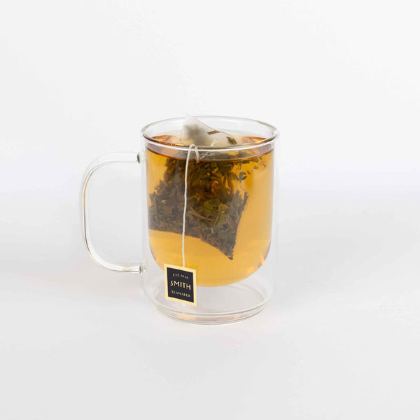 Clear glass mug with tea being brewed, featuring a tea bag with a label on a white background.