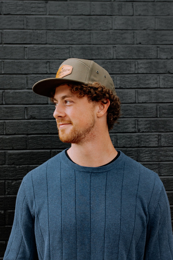 Man wearing a green cap and blue sweater against a black brick wall