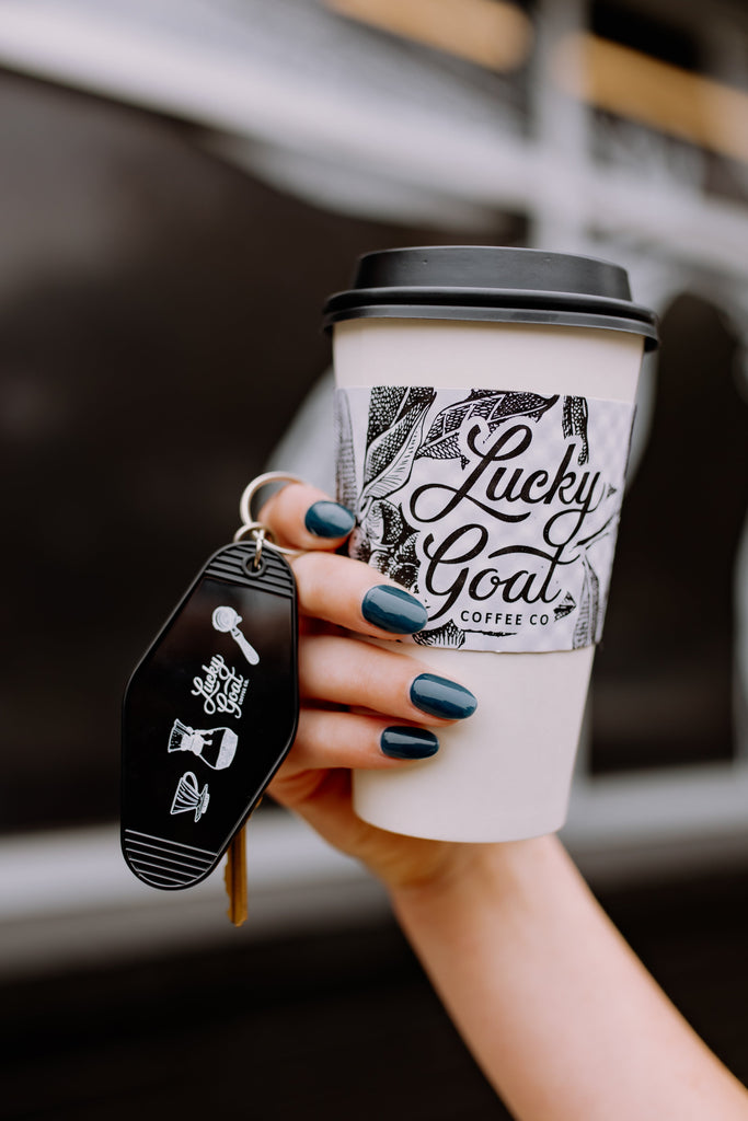 Hand holding a coffee cup with 'Lucky Goat Coffee Co.' branding, blurred background