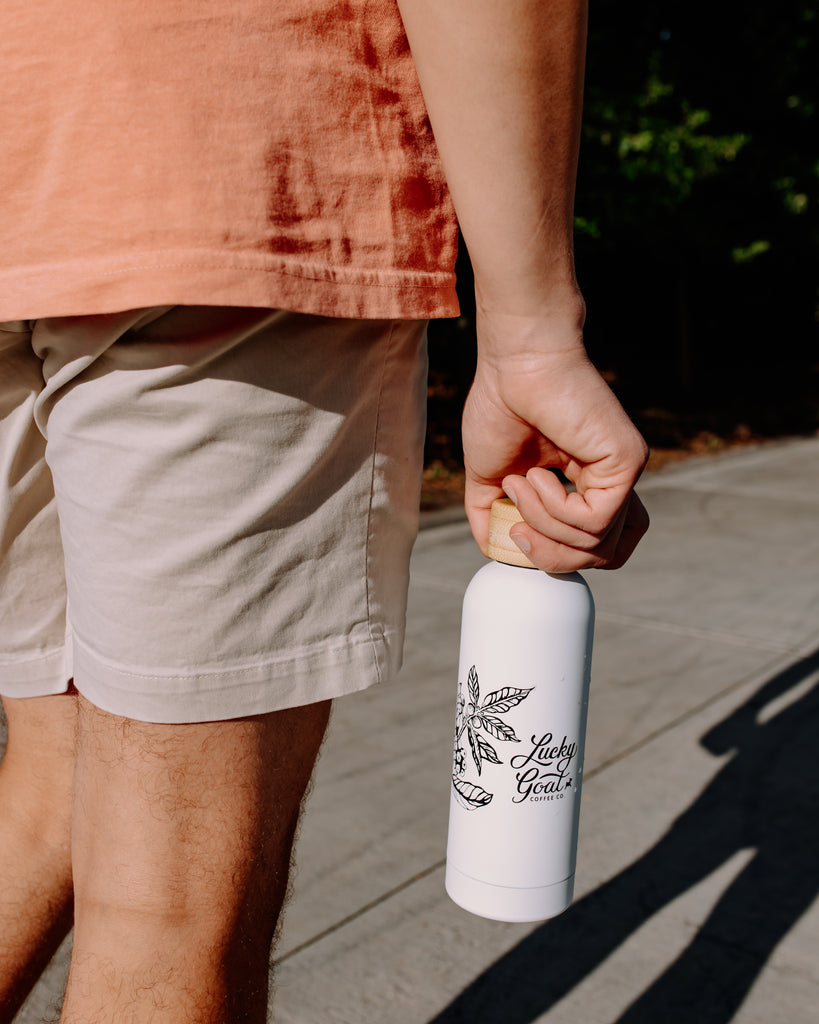 Person holding a white water bottle with black text and design, wearing an orange shirt and beige shorts.